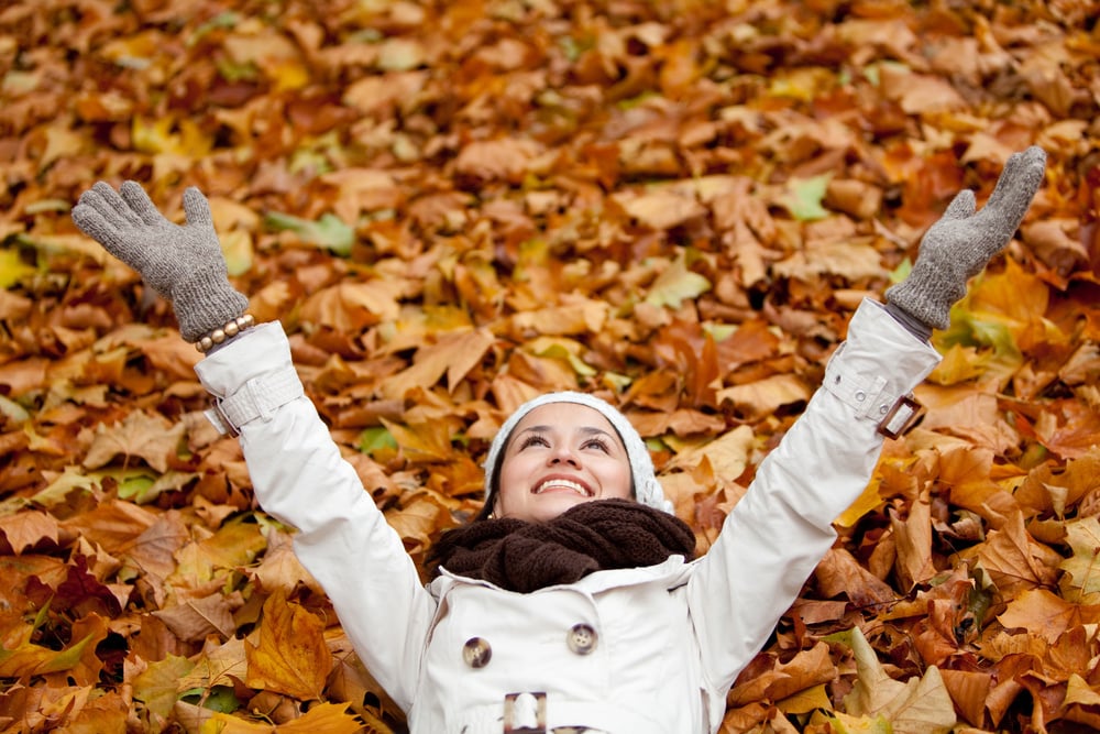 Happy autumn woman lying over leaves and smiling